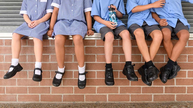 school students sitting on a wall showing school shoes